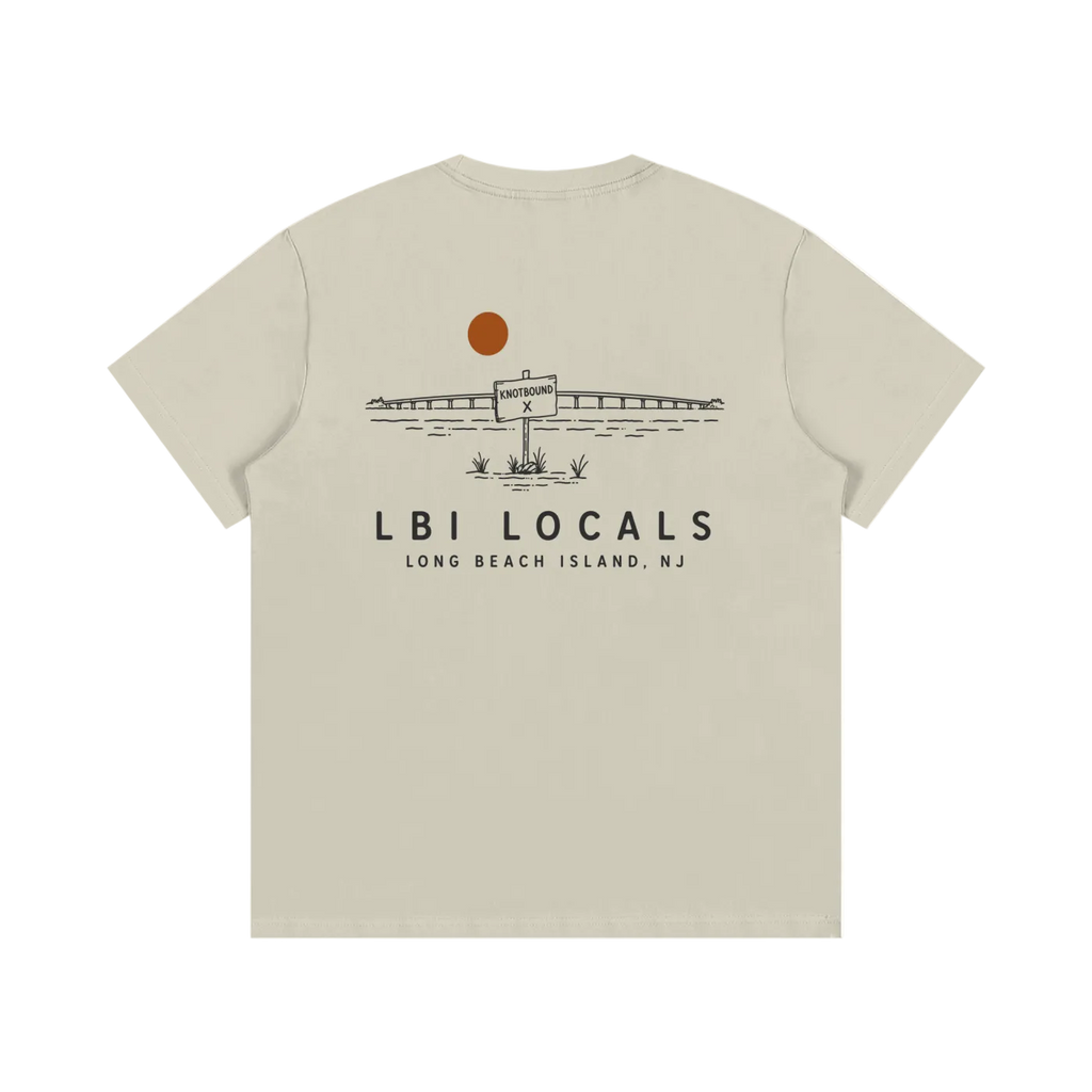 A beige short-sleeve t-shirt shown from the back, featuring a black line art graphic of a seaplane at a lighthouse with an orange sun and the text 'LBI LOCALS' and 'LONG BEACH ISLAND, NJ'.