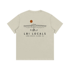 A beige short-sleeve t-shirt shown from the back, featuring a black line art graphic of a seaplane at a lighthouse with an orange sun and the text 'LBI LOCALS' and 'LONG BEACH ISLAND, NJ'.