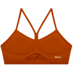 A rust-orange sports bra with a crossover criss-cross back strap design and a small white script logo on the lower right side, displayed against a solid white background.