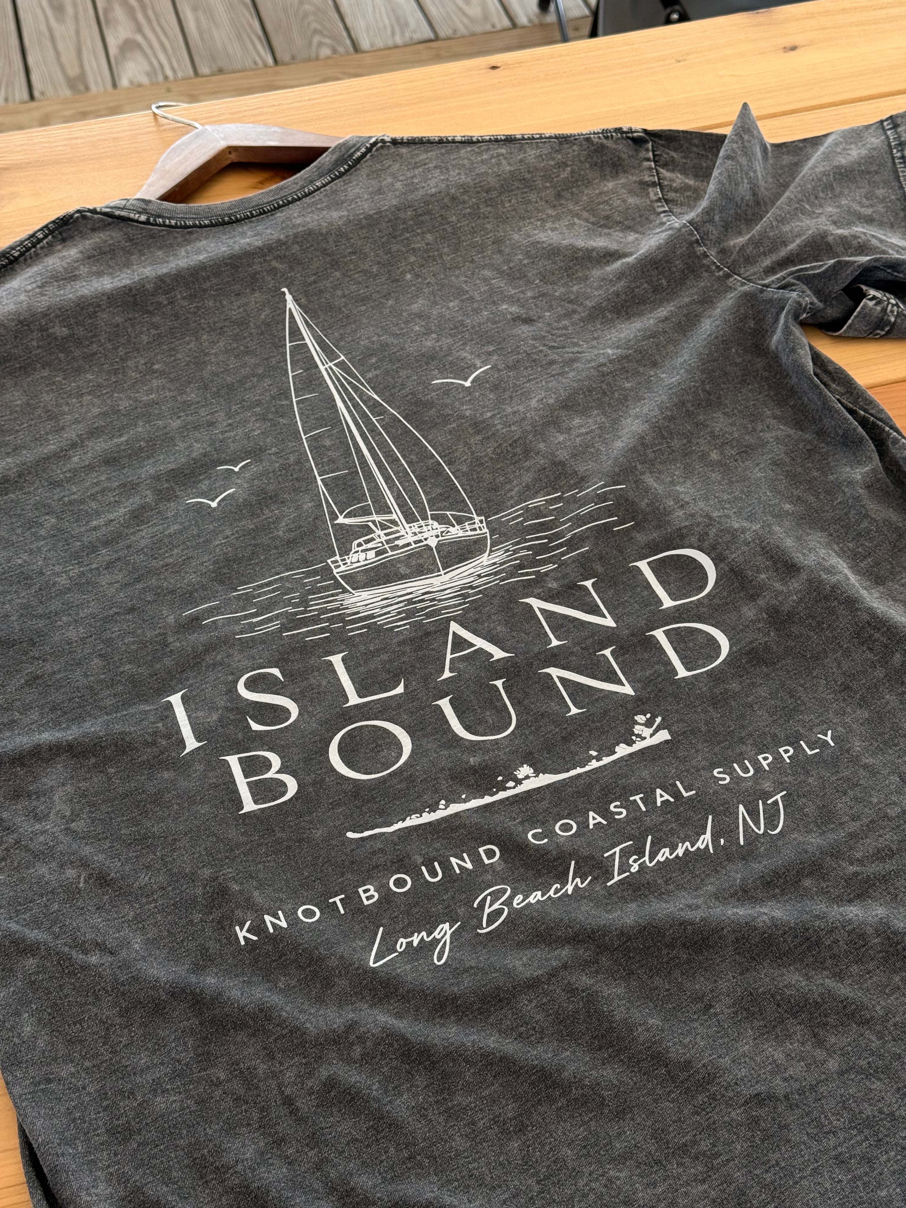 The Knotbound Island Bound Stonewash Tee laid flat on wood, showing the sailboat back graphic and Long Beach Island, NJ text.