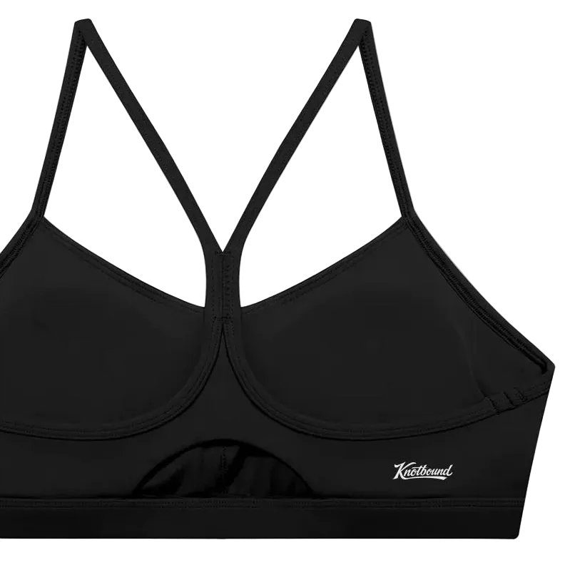 A black sports bra with a crossover criss-cross back strap design and a small white script logo on the lower right side, displayed against a solid white background.